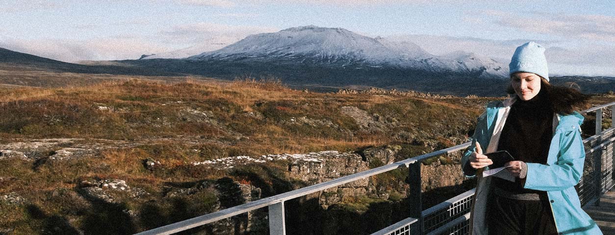 En medarbetare på Devize promenerar med en mobiltelefon, med en karg slätt och snöklädda berg i bakgrunden