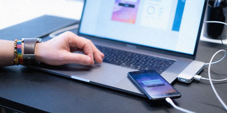 Närbild på hand vid laptop och mobiltelefon